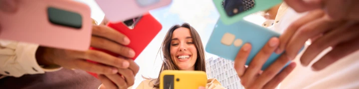 Fröhliches Mädchen schaut auf Smartphone. Gruppe von Freunden mit Handys